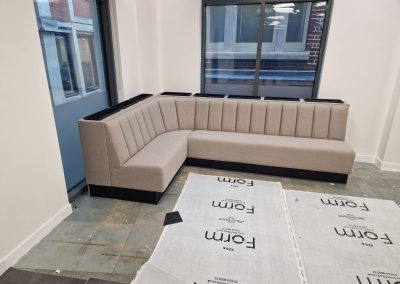 L-shaped wall bench seating with integrated planter capping and matching upholstery, set against a vertical slatted wood wall in a contemporary office or lounge space.