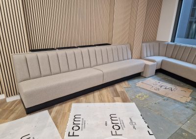 Wall bench seating with integrated planter capping and matching upholstery, set against a vertical slatted wood wall in a contemporary office or lounge space.